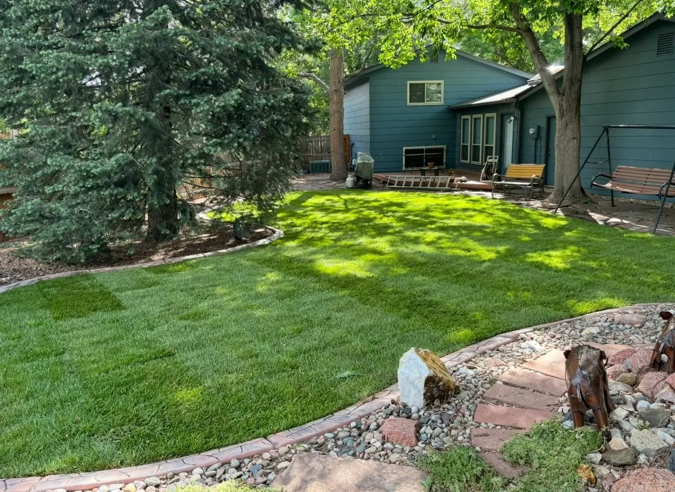 Backyard lawn with stone edging and mature trees behind a teal house